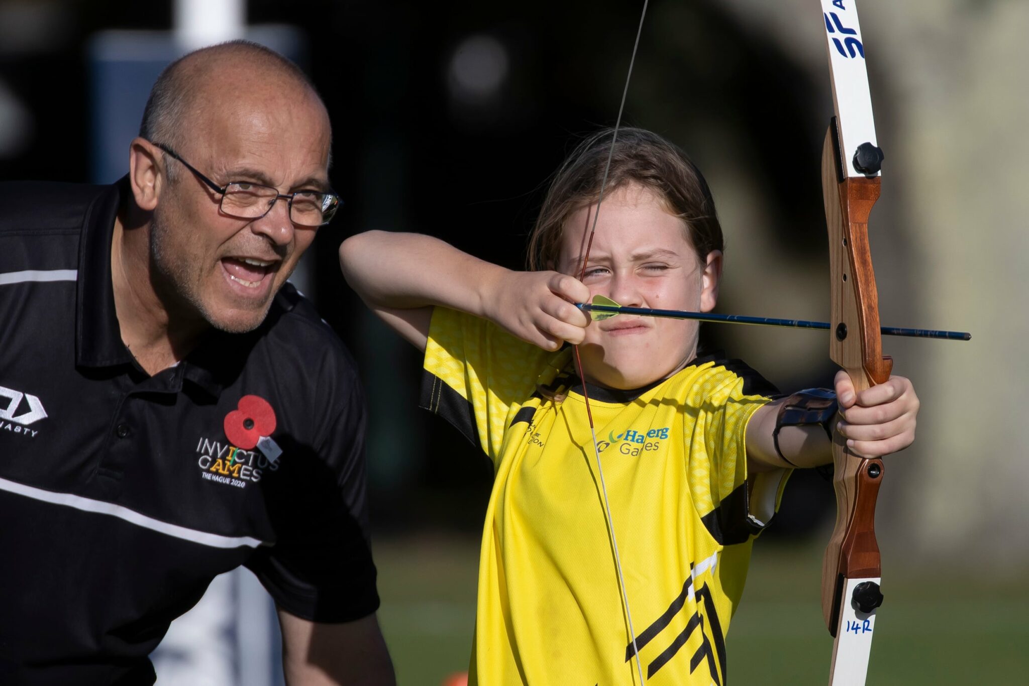 Young girl in bright yellow t-shirt shoots bow and arrow