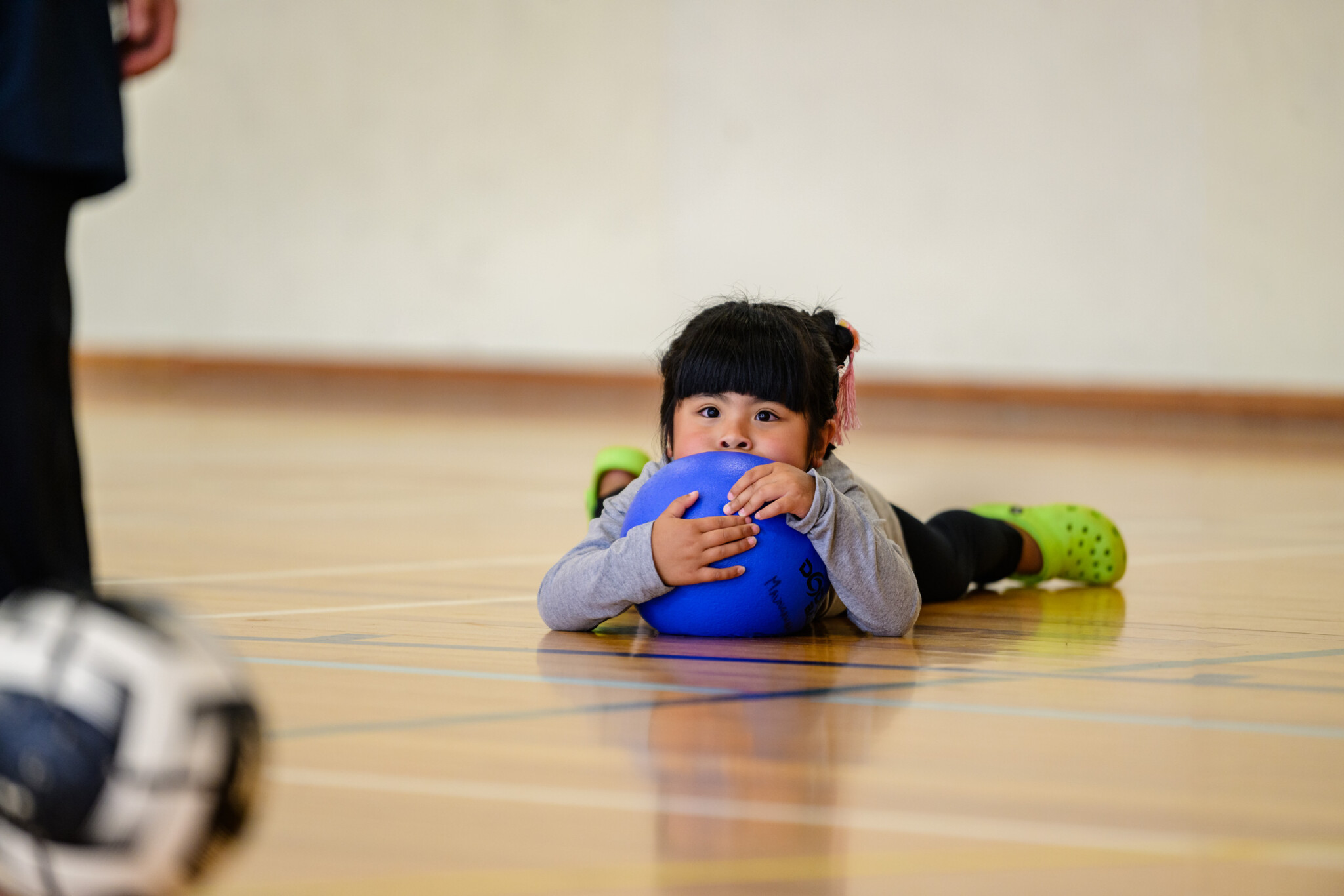 young girl lying on school gymnasium floor with her arms wrapped around a blue ball